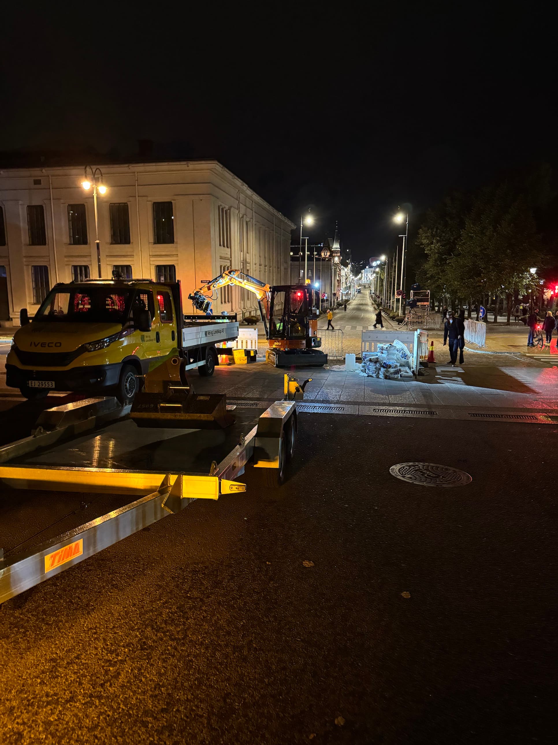 Minigraver og lastebil ved steinarbeider i bysentrum om kvelden